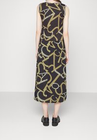 Maxikleid in Schwarz mit großen goldenen Buchstaben und grünen Akzenten. Ärmelloses Design mit lockerer Passform, das einen ausgestellten Saum und eine glatte Textur aufweist.