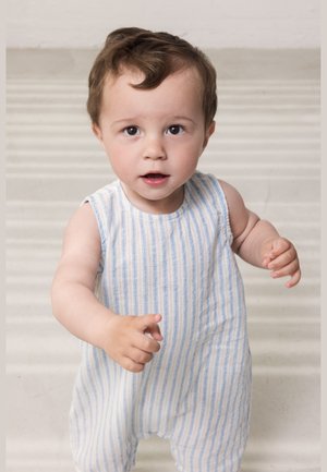 Tout-petit aux cheveux châtain clair portant une combinaison sans manches à rayures bleues et blanches, tendant les deux mains vers l'avant.