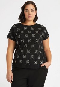 Top negro de manga corta con un patrón geométrico y acentos plateados. Fabricado en tejido suave con un ligero brillo y un diseño de corte relajado.