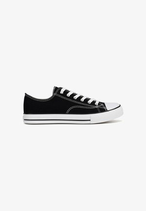 Zapatilla negra de lona baja con puntera de goma blanca, cordones blancos, suela blanca y costuras blancas a contraste vista de perfil sobre fondo blanco.