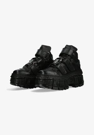 Baskets en cuir noir avec une semelle en caoutchouc épaisse, dotées de deux sangles Velcro, de panneaux texturés et d'un motif de crampons prononcé.