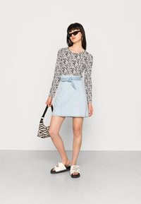 Blusa de manga longa com padrão de zebra em preto e branco, saia em denim azul claro em formato A com detalhes em laço, mala com padrão de zebra em preto e branco, sandálias brancas.