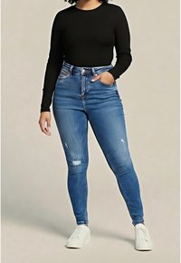 Femme portant un haut noir à manches longues, un jean skinny bleu déchiré taille haute, des baskets blanches, debout avec une main dans la poche.