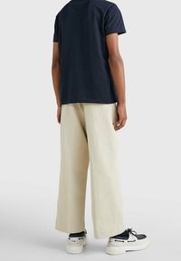 Marinblå bomull t-shirt med avslappnad passform, kombinerad med krämfärgade vida byxor och svarta sneakers med vit sula och snörning.