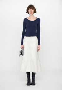 Marineblaues Langarmoberteil, weißer Jeansrock in A-Linie, schwarze kniehohe Stiefel und silberne Handtasche. Glatte Texturen mit lässigem Design.