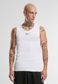 Hvit ribbed tanktop med en buet halslinje og en liten svart logo på brystet. Laget av lett bomullsstoff.