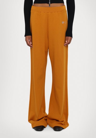 Pantaloni largi dintr-un material galben muștar cu o textură netedă, având un brâu elastic și un detaliu decorativ subtil pe șold.