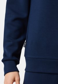 Felpa blu navy con una texture liscia, polsini a coste e un'etichetta del marchio visibile sul lato vicino all'orlo.