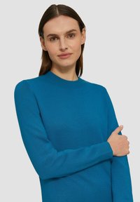 Turkusowy sweter z długim rękawem, okrągłym dekoltem, ściągaczami na rękawach oraz miękką fakturą. Posiada dopasowany krój i minimalistyczny design.