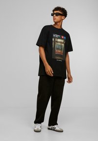 Sort oversized t-shirt med et grafik af en subway-skylt, parret med løse sorte bukser og hvide sneakers med grå og sorte detaljer.