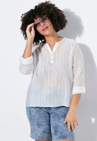 Blusa blanca ligera con diseño de rayas transparente, mangas tres cuartos y escote abotonado, combinada con pantalones cortos de mezclilla.