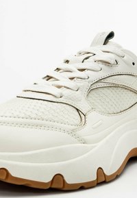 Sneaker bianca con pelle testurizzata e accenti sintetici lisci. Dotata di suola spessa e design con lacci, presenta un mix di motivi.
