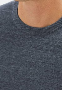 Pull gris foncé avec un motif en maille texturée, présentant un col rond classique et des bords lisses. Vue en gros plan mettant en valeur la qualité du tissu.