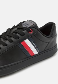 Černé kožené tenisky s červenými, bílými a modrými pruhy, černými tkaničkami a brandingem Tommy Hilfiger na boku a jazyku.