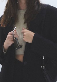 Black blazer with 2 buttons, ribbed light beige crop top, and clear eyewear held in hand, showcasing a minimalistic design.