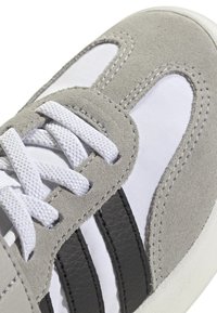 Sneaker in suede grigio con pannelli in rete bianca, strisce nere e lacci bianchi. Presenta una superficie testurizzata e una punta arrotondata.