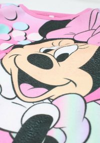 T-shirt en tissu rose avec un grand design de personnage de dessin animé, texture douce, accents noirs et roses, et des points de couleur pastel en arrière-plan.
