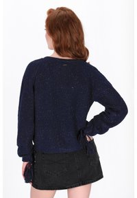 Granatowy sweter dzianinowy o teksturowanym wykończeniu i luźnym kroju. Posiada wiązania na rękawach i okrągły dół, w zestawieniu z czarną spódnicą dżinsową.