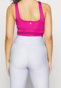 Fuchsiová sportovní podprsenka se širokými ramínky a kulatým výstřihem na zádech. Světle levandulové legíny s hladkou, elastickou texturou a minimálním značením.