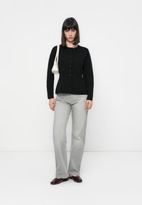Cardigan tricotat negru, cu nasturi, cu mâneci lungi, asortat cu blugi gri deschis cu croială evazată. Accesoriile includ o geantă mică albă și pantofi închiși la culoare.