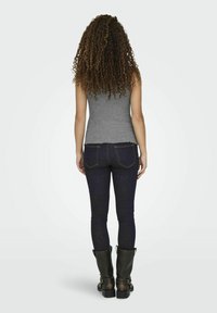 Grå tætsiddende tanktop parret med mørkeblå skinny jeans og sorte knæhøje støvler med metaldetaljer, set fra ryggen.