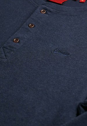 Marineblauwe henley-shirt met drie bruine knopen en subtiele geborduurde logo op de linkerborst.