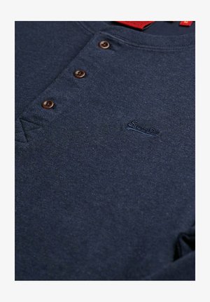 Marineblå henley skjorte med tre brune knapper og subtilt broderet logo på venstre brystområde.