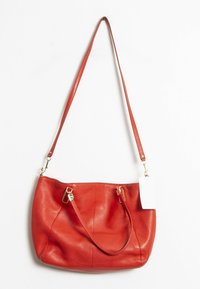 Sac à main en cuir rouge au design décontracté, avec une longue sangle ajustable, des accents en métal doré et une étiquette attach�ée. Texture lisse avec des détails plissés.