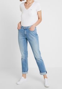 Vit kortärmad T-shirt med V-ringning i kombination med ljusblå jeans med uppvikta ben och vita sneakers, med en klassisk passform och mjukt material.