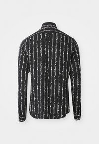Zwart shirt met lange mouwen met een wit verticaal prikkeldraadpatroon. Gemaakt van lichte stof met een klassieke kraag en knoopsmanchetten.