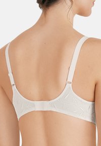Reggiseno beige chiaro in materiale liscio, con ricami floreali, spalline regolabili e chiusura a gancio sulla schiena, dotato di scollatura rotonda.