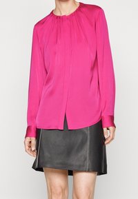 Fuchsia Seidenbluse mit Rundhalsausschnitt, langen Ärmeln und Vorderfalten; kombiniert mit einem schwarzen Lederrock mit weißen Nähten.
