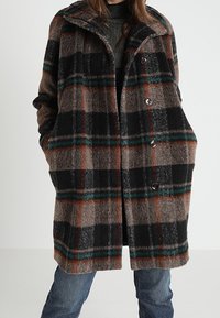 Ternet uldfrakke med stor krave i brune, sorte og grønne farver, med markant ternet mønster og to knapper foran.