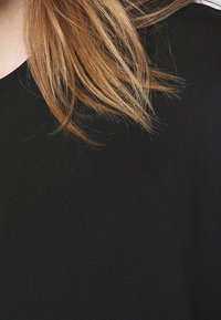 Sort stof med en glat tekstur, der viser lange brune hårstrå delvist. Beklædningen har en løs, rund halsudskæring og korte ærmer.