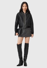 Giacca bomber in pelle nera con borchie argentate, abbinata a una minigonna borchiata e stivali alti in pelle nera. Design elegante e aderente.