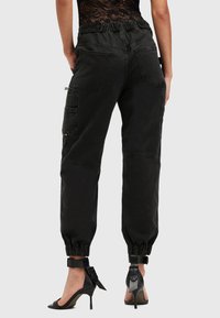 Zwarte cargobroek met elastische taille en enkelboorden, met zijzakken en een duurzame stof. G gedragen met zwarte hoge hakken.