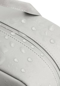 Tessuto impermeabile grigio con una texture liscia, caratterizzato da gocce d'acqua e un dettagli di cucitura a contrasto; progettato con linee curve e una tracolla resistente.
