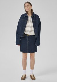 Ensemble en denim composé d'une veste et d'une jupe bleu foncé, avec un T-shirt rayé blanc en dessous. Des baskets marron et des chaussettes blanches complètent la tenue.