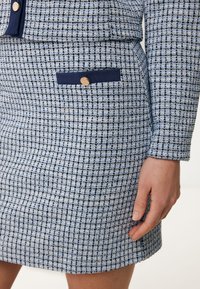 Gonna in tessuto a quadri blu e bianchi con una piccola tasca navy e bottone in legno. Design testurizzato, aderente, con orlo dritto.