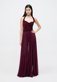 Rochie bordo cu decolteu tip halter, cu corsaj adunat și fustă semi-transparentă fluidă, realizată dintr-un material ușor, ce oferă o textură fină.