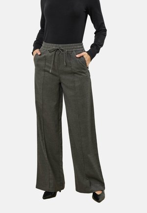 Femme portant un pantalon gris à jambes larges avec une taille élastique et un cordon de serrage, un haut noir à manches longues et des chaussures noires à bout pointu.