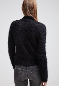 Czarny, puszysty sweter dzianinowy z długimi rękawami, wysokim kołnierzem i teksturowanym wykończeniem. Posiada dopasowaną talię oraz widoczne szwy na plecach.
