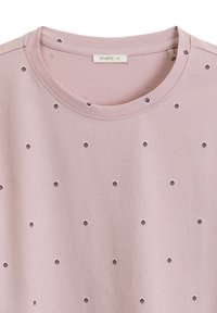 Jasnoróżowa koszulka z krótkim rękawem, z okrągłym dekoltem i regularnie rozmieszczonymi heksagonalnymi wycięciami w całym materiale. Gładka tekstura.