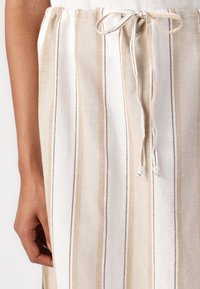 Shorts en tissu coton avec des rayures verticales beige et blanches. Ils présentent une taille élastique avec un cordon de serrage et des perles décoratives.