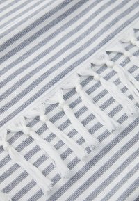 Håndkle med stripet mønster i hvit og marineblå, med hvite duskler langs den ene kanten for pynt. Myk tekstur og vevet materiale.