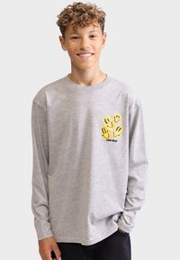 Graues Langarm-T-Shirt aus Baumwolle mit einem gelben Grafikdesign von lächelnden Gesichtern auf der linken Brust. Einfacher, lässiger Schnitt.