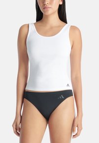 Débardeur blanc côtelé avec de larges bretelles, associé à un bas de bikini noir arborant un petit logo. Le débardeur est ajusté et possède une texture lisse.