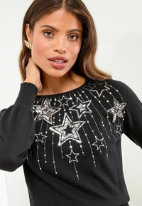 Maglione nero con un design impreziosito da stelle di paillettes argentate e dettagli in perline, con maniche lunghe a sbuffo e scollatura rotonda.