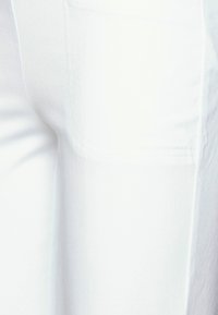 White denim pants with a smooth texture, featuring a side pocket and subtle stitching details. The design is fitted and tapered.