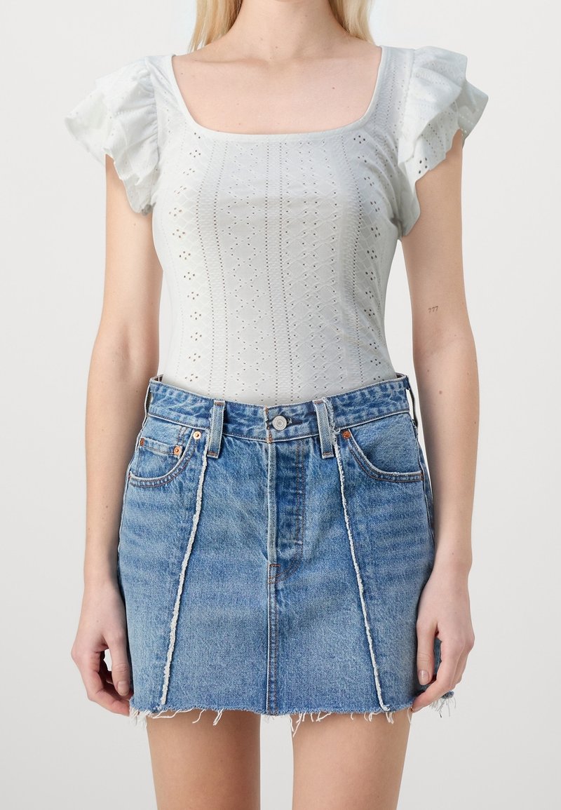 Light gray cotton top with ruffled sleeves and eyelet pattern, paired with a denim mini skirt featuring a frayed hem and front seams.